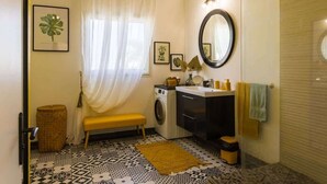 A compact bathroom with a washing machine, a sink, a mirror, and a bench. - Kaz Zévi - Haut de Villa 4* à la Saline les Bains (Saint-Paul)