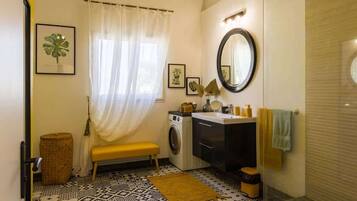 Une petite salle de bain équipée d’un lave-linge, d’un évier, d’un miroir et d’un banc.