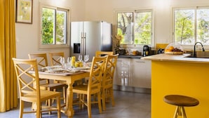 A bright kitchen with yellow accents, a dining area with wooden chairs, and large windows offering views of greenery. - Kaz Zévi - Haut de Villa 4* à la Saline les Bains (Saint-Paul)