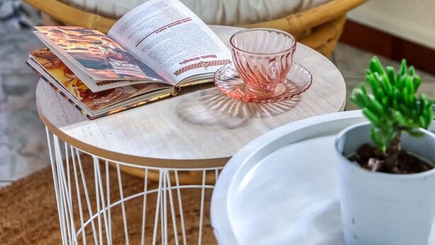 Un coin lecture confortable avec un fauteuil moelleux, une petite table ronde sur laquelle sont posés un livre et un verre, et une plante en pot.