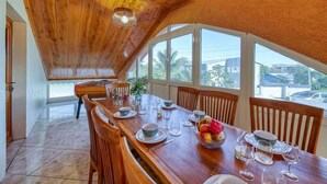 Un coin repas avec une table en bois dressée pour six personnes, entourée de chaises, et une grande fenêtre offrant une vue sur l’extérieur.