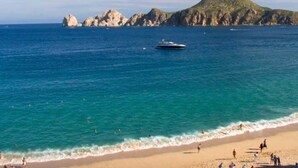 Una playa con agua azul cristalina, un bote y acantilados rocosos al fondo.