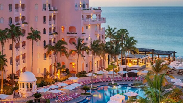 Un resort con una piscina grande, palmeras y vista al océano.