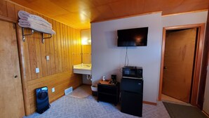 A compact room with wooden paneling, a mounted TV, a small kitchenette, and a door. - Northwoods Lodge Hotel Room 2 (Long Lake)