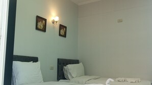 A hotel room with two beds, a dark headboard, a light-colored wall, and two wall-mounted light fixtures. - New Panorama Palace (Cairo)