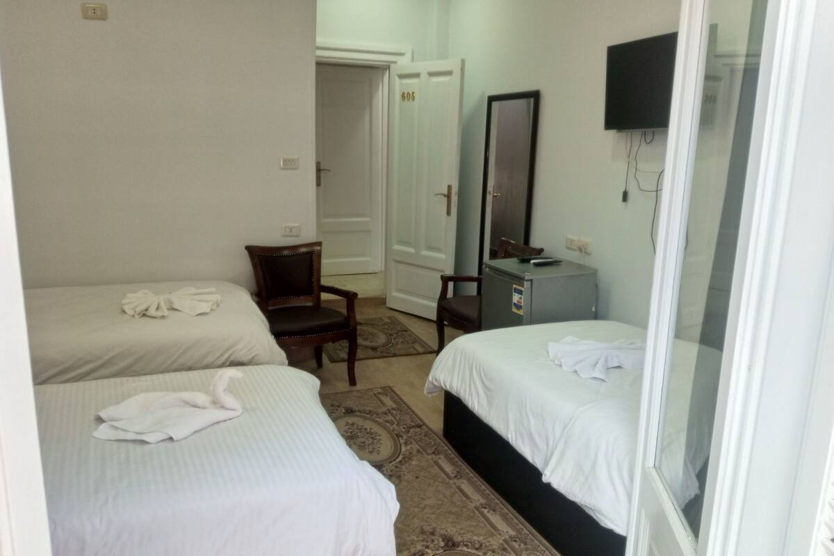 A hotel room with two beds, a chair, a desk, a mirror, and a television.