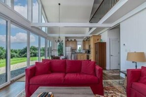 A spacious living area with a red sofa, a coffee table, and a view of a kitchen and outdoor landscape. - Blueberry Hill Cottage, Lexington Virginia, Blueberry Hill Cottage, Lexington Virginia (Lexington)
