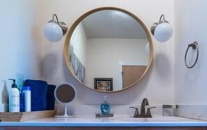 A bathroom with a round mirror, two wall-mounted lights, a sink, and toiletries. - Blueberry Hill Cottage, Lexington Virginia, Blueberry Hill Cottage, Lexington Virginia (Lexington)