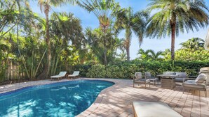 A swimming pool with lounge chairs and a patio area surrounded by palm trees and greenery.