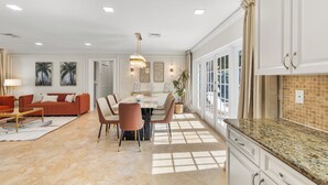 A spacious living room with a red sofa, a dining area with a white table, and a kitchen with white cabinets and a granite countertop.