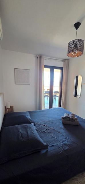 A bedroom with a bed, a bedside lamp, a framed picture, a window with curtains, and a hanging light fixture. - Magnificent seaside apartment with terrace and sea view. (Pietrosella)