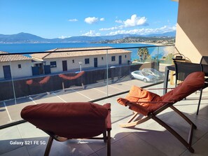 A balcony with a view of a coastal town, a parked car, and a Galaxy S21 FE 5G smartphone. - Magnificent seaside apartment with terrace and sea view. (Pietrosella)