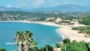 Un paysage côtier avec une plage, des palmiers et des montagnes à l’horizon.