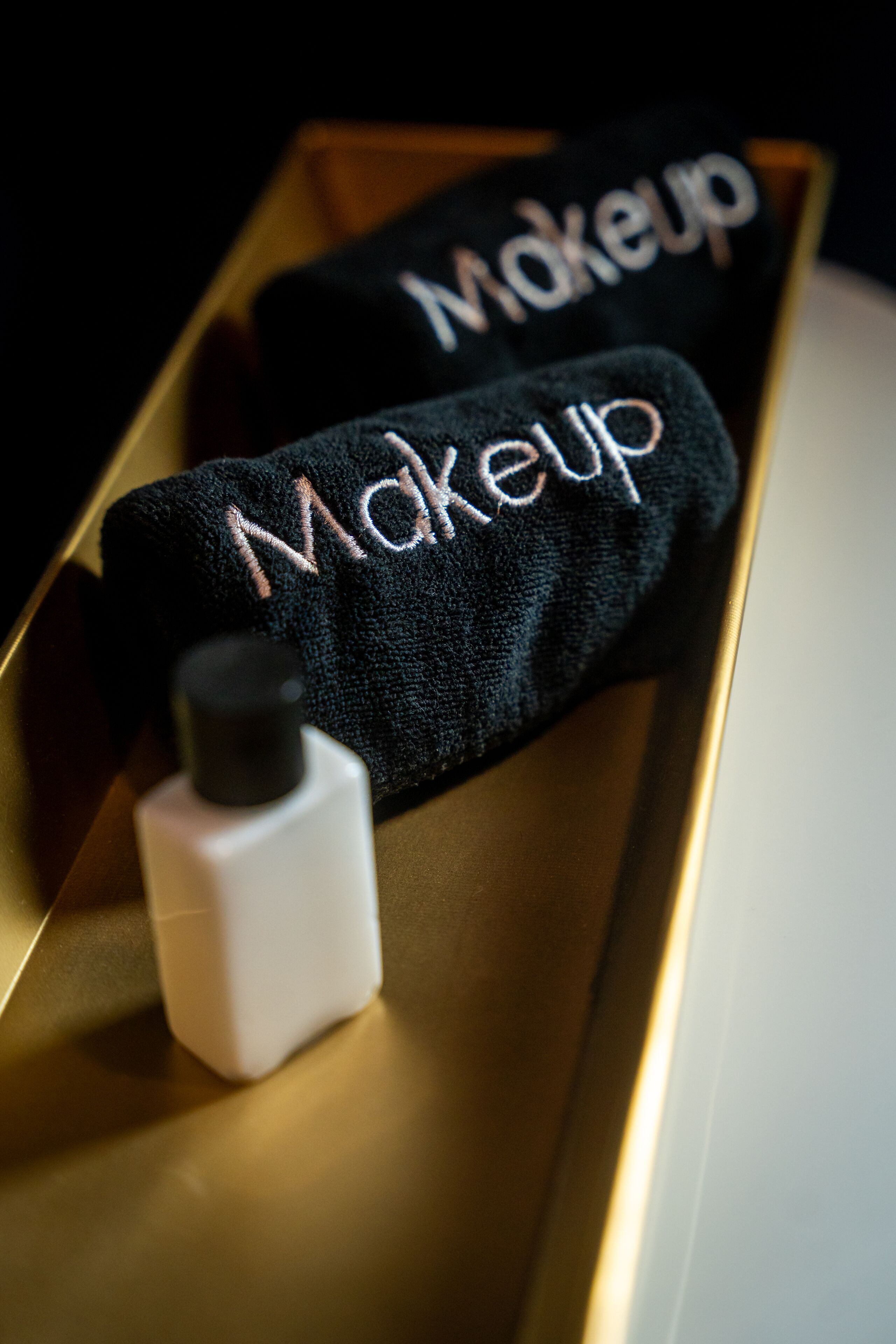 Un asciugamano per il trucco con la scritta "Makeup" ricamata, appoggiato su un vassoio accanto a una bottiglia.
