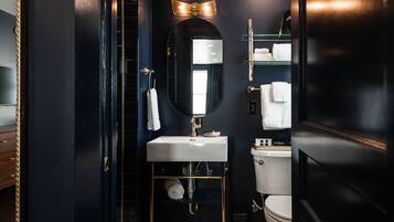 Een moderne badkamer met een donkere inrichting, voorzien van een wit wastafelmeubel, een spiegel met verlichting erboven en een toilet.