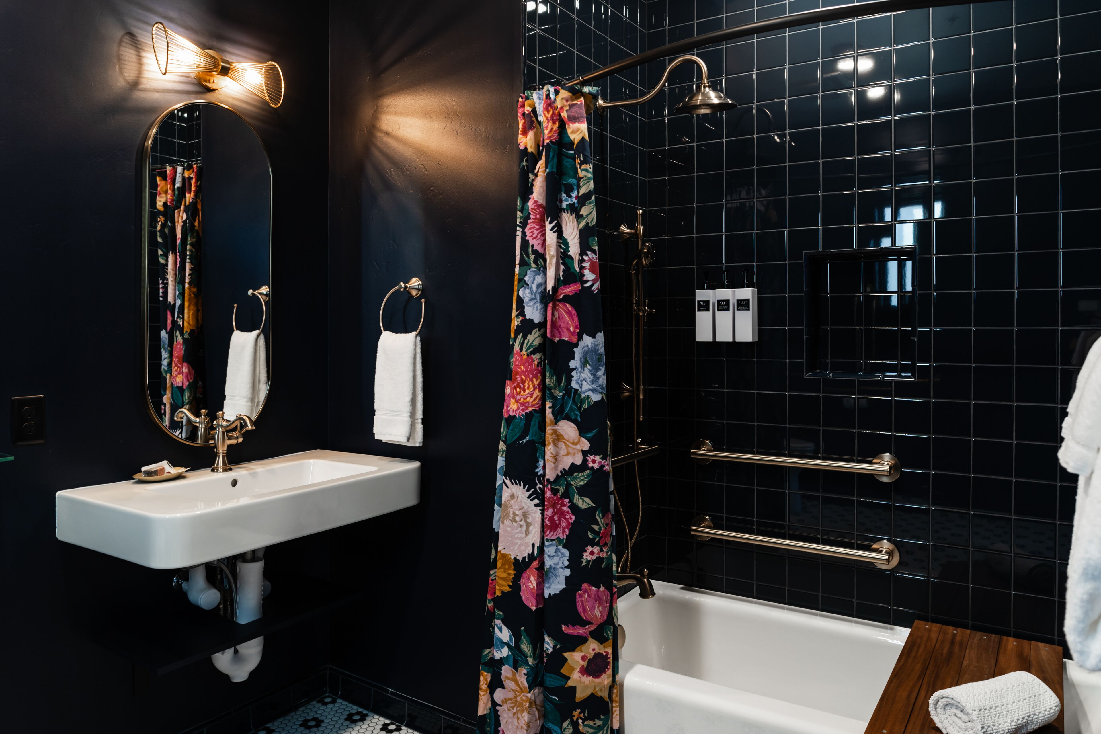 A modern bathroom with a white sink, a mirror, a shower curtain with floral patterns, and a bathtub.