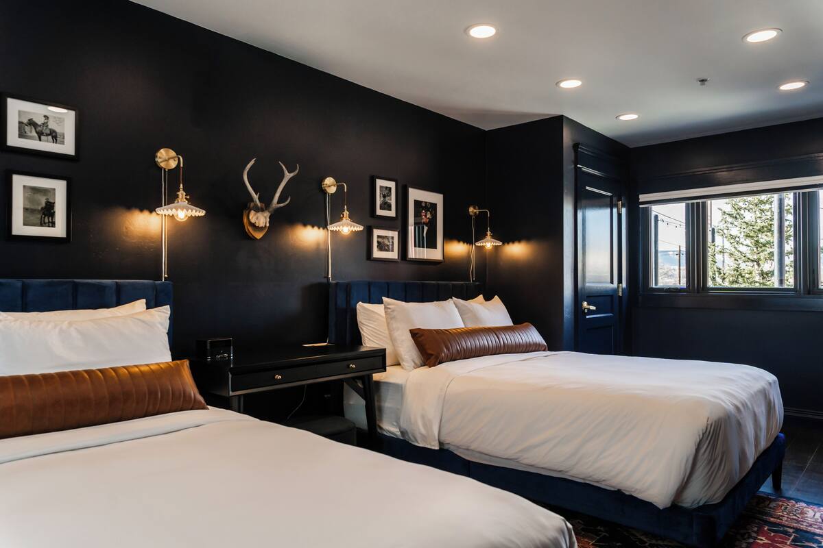 A modern hotel room with two beds, dark walls, and framed pictures.
