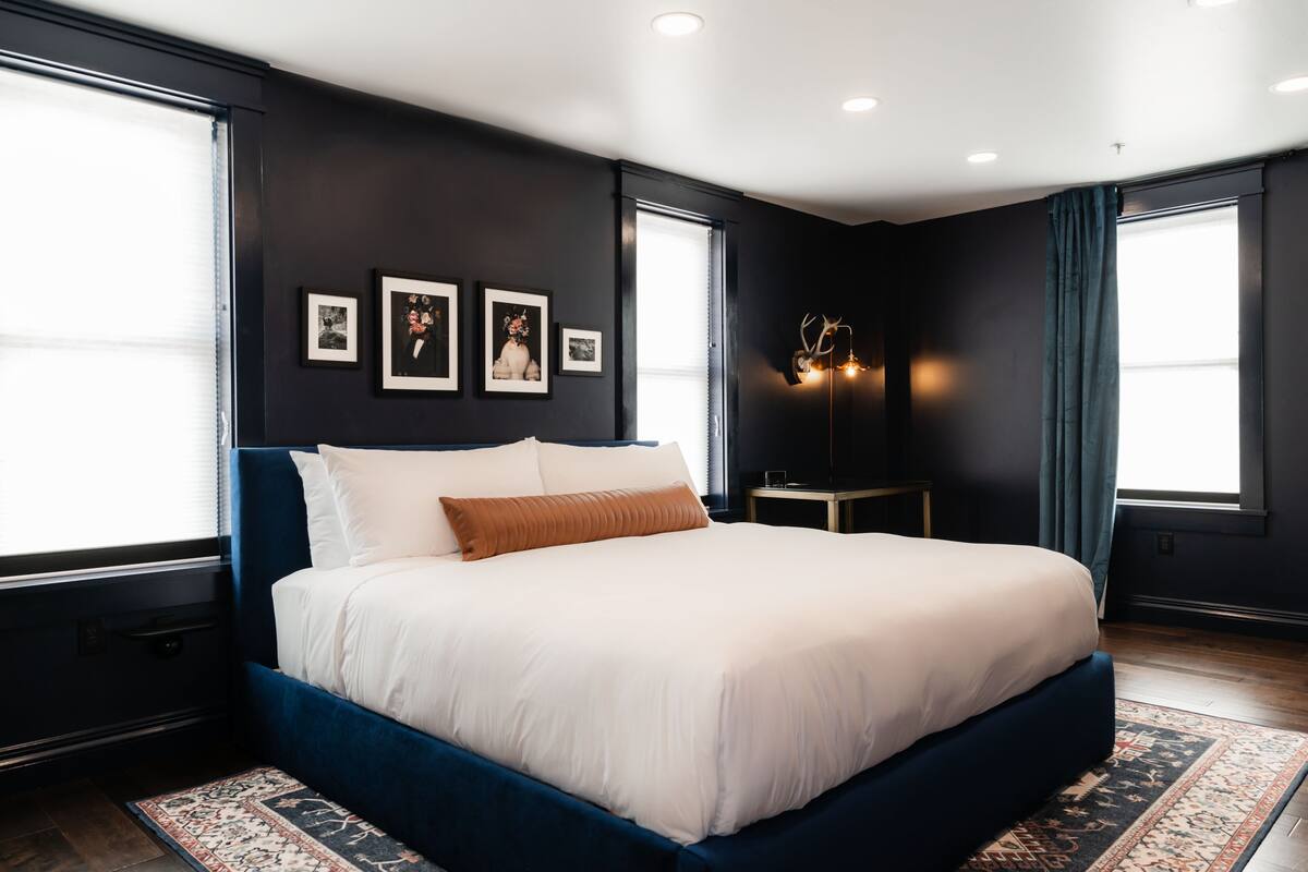A modern bedroom with a large bed, dark walls, and framed pictures on the wall.