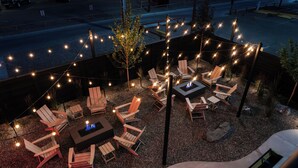 An outdoor seating area with multiple Adirondack chairs and a central fire pit. - The Hotel Melrose (Grand Junction)