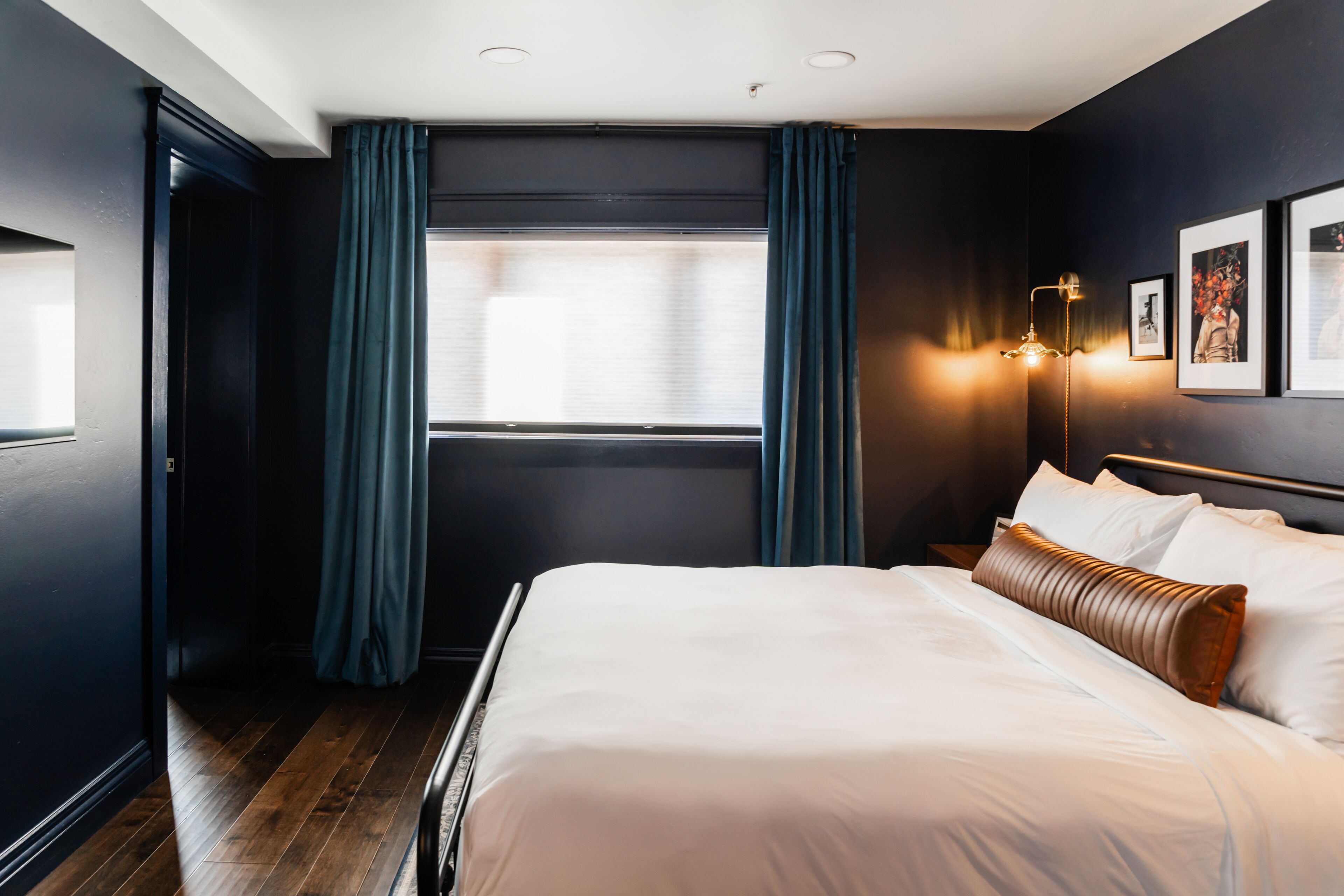 A modern hotel room with a large bed, dark walls, and a window with curtains.