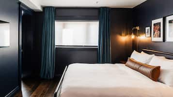 A modern hotel room with a large bed, dark walls, and a window with curtains.