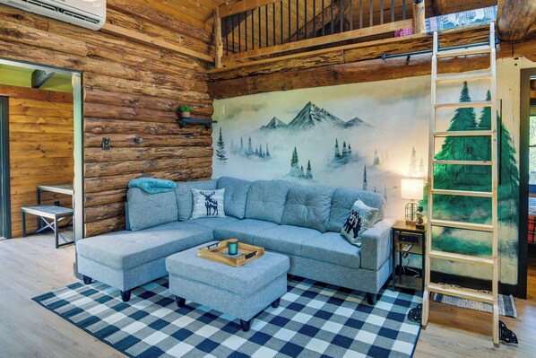 A cozy log cabin interior with a sectional sofa, a checkered rug, and a mountain mural on the wall. - Fairhaven Harbor-Front Gem - Steps From the Water! (Fairhaven)