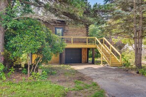 A log cabin with a wooden staircase leading to a balcony, surrounded by trees and greenery. - Fairhaven Harbor-Front Gem - Steps From the Water! (Fairhaven)