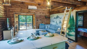 A log cabin interior with a dining area, a sofa, a ladder, and a painting of a mountain scene. - Fairhaven Harbor-Front Gem - Steps From the Water! (Fairhaven)