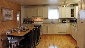 Una cocina con suelo de madera, armarios blancos, una mesa de comedor con sillas y un ventilador de techo.