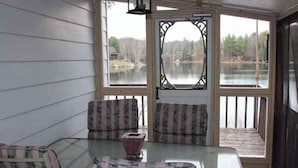 Un patio techado con una mesa de vidrio y dos sillas a cuadros, con vista a un lago.