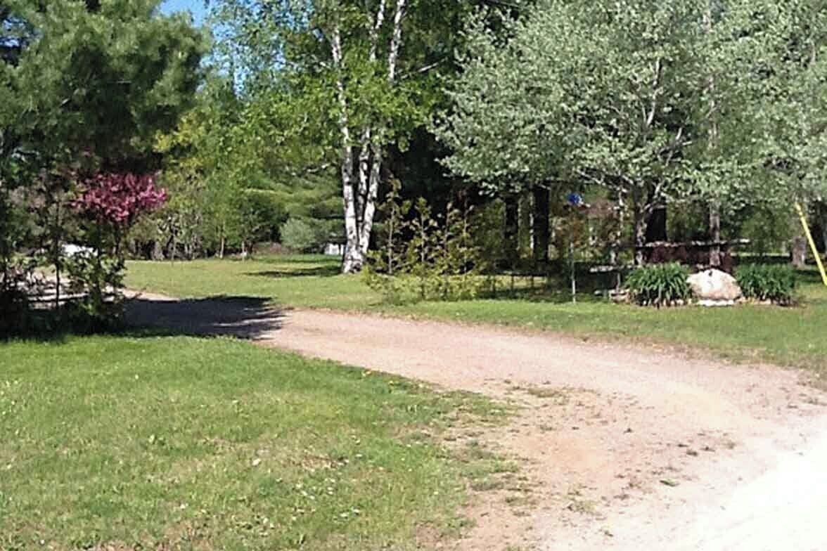 Un sentier de terre qui traverse une zone herbeuse, parsemée d’arbres et d’arbustes.
