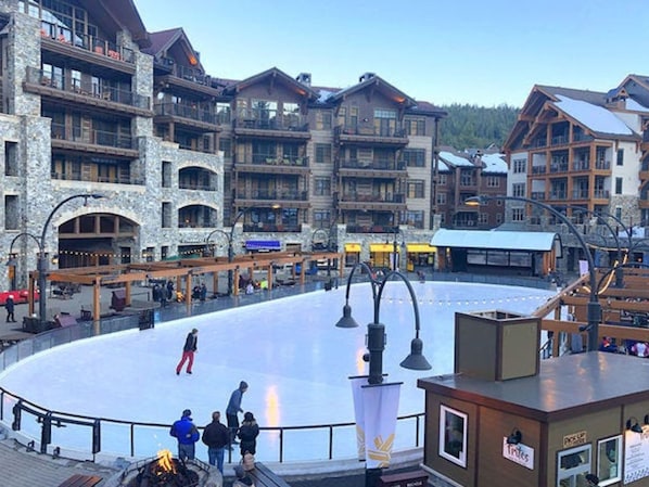 A large indoor ice skating rink surrounded by multi-story buildings with stone facades and balconies.