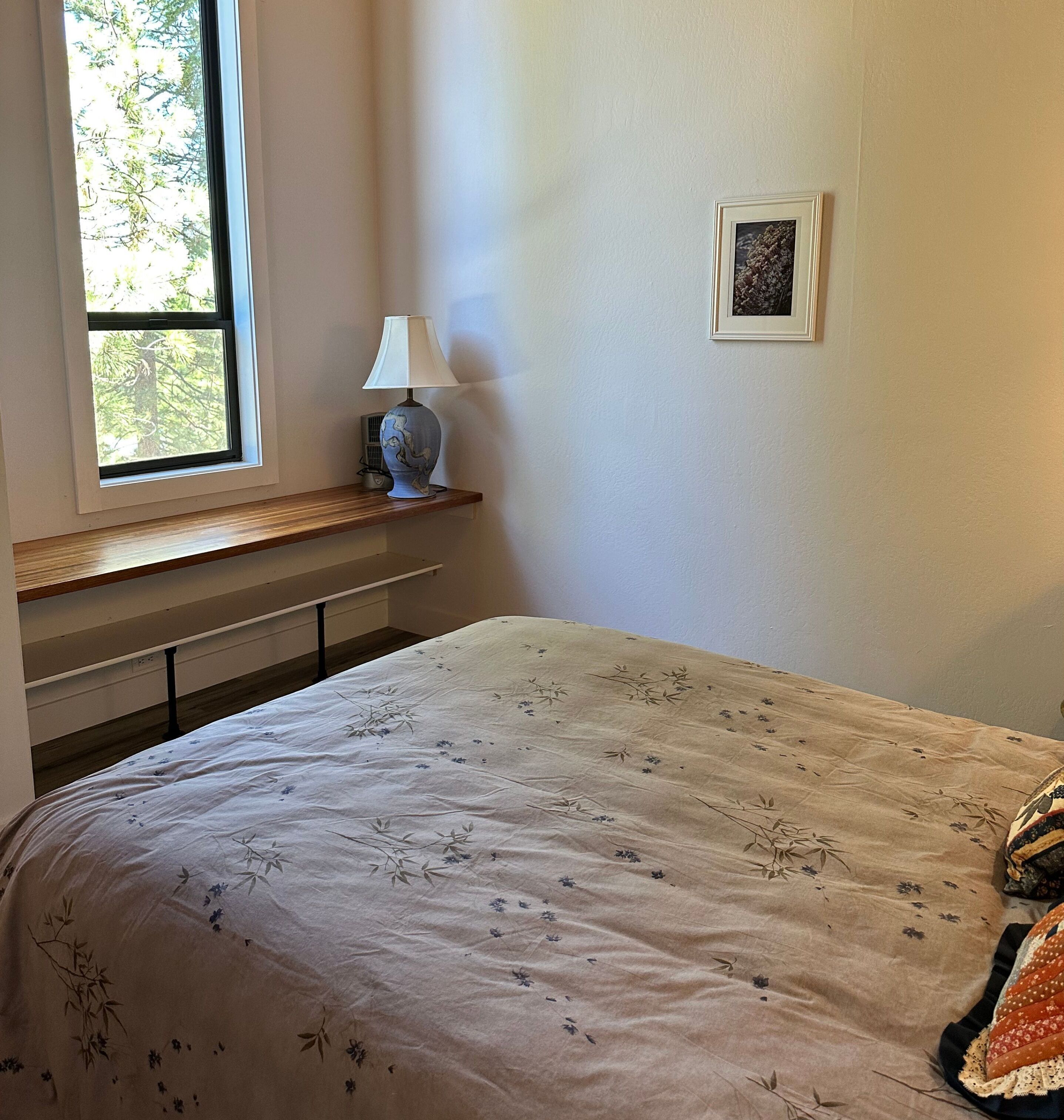 Un dormitorio con una cama, una ventana, una lámpara y un cuadro en la pared.