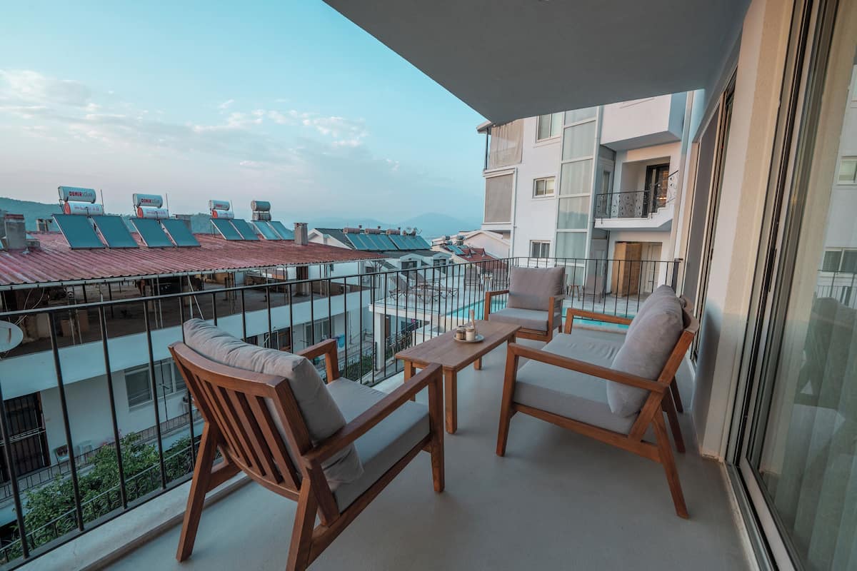 Un balcon doté de mobilier en bois, d’une rambarde en verre et offrant une vue sur d’autres immeubles et sur une étendue d’eau.
