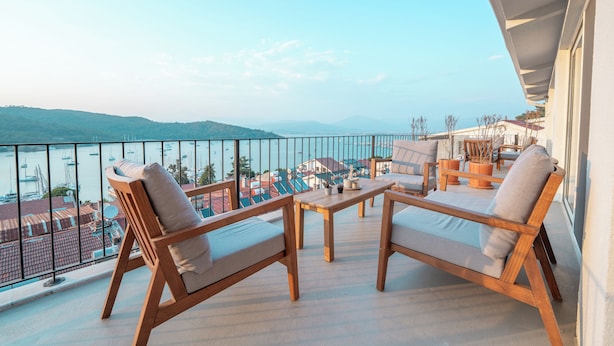 Ein Balkon mit Holzmöbeln, einem Tisch und Blick auf das Meer und Gebäude.