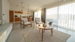 Ein modernes Wohnzimmer mit einem runden Holztisch, zwei Stühlen, einer Couch und einem Küchenbereich im Hintergrund.