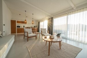 Una sala moderna con una mesa redonda de madera, dos sillas, un sofá y una cocina al fondo.
