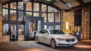 En vit BMW 7-serie är parkerad inuti en byggnad med stora fönster och väggar av sten.