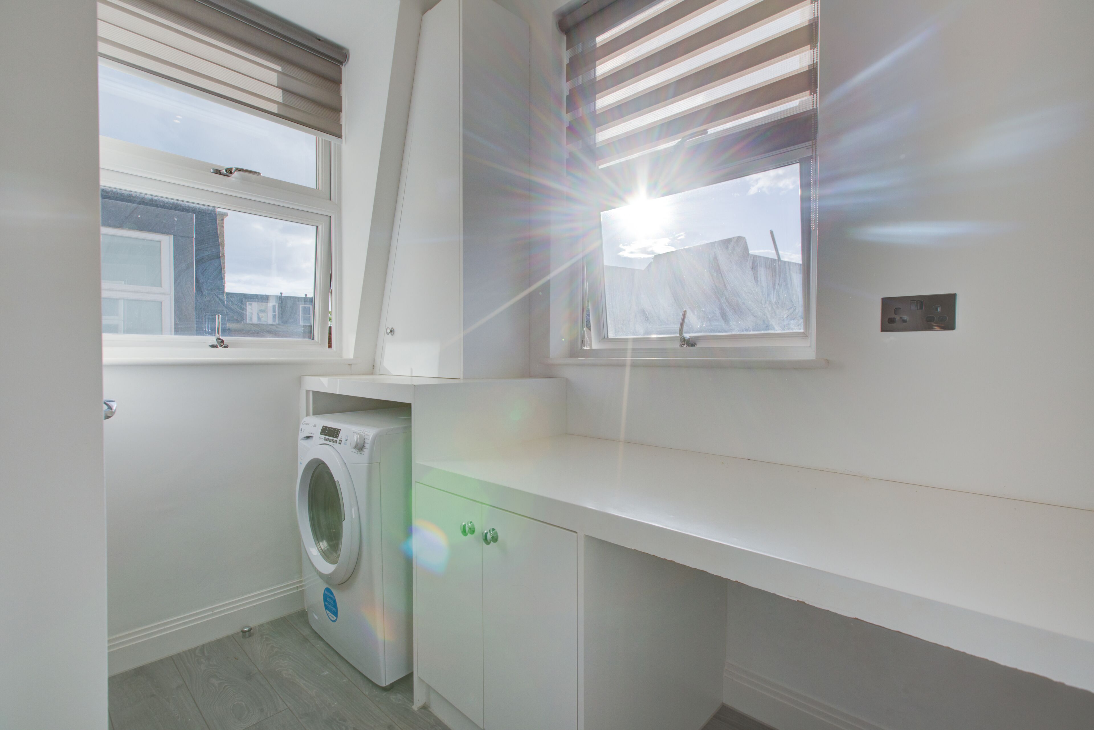 A laundry room with a washing machine, a sink, and a window with blinds.