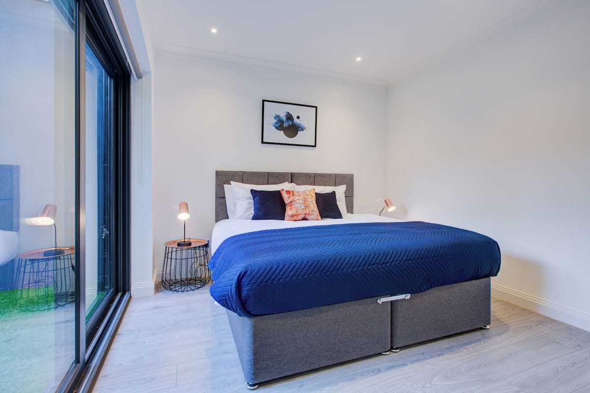 Quarto moderno com cama grande, porta de vidro para uma varanda e uma obra de arte emoldurada na parede.