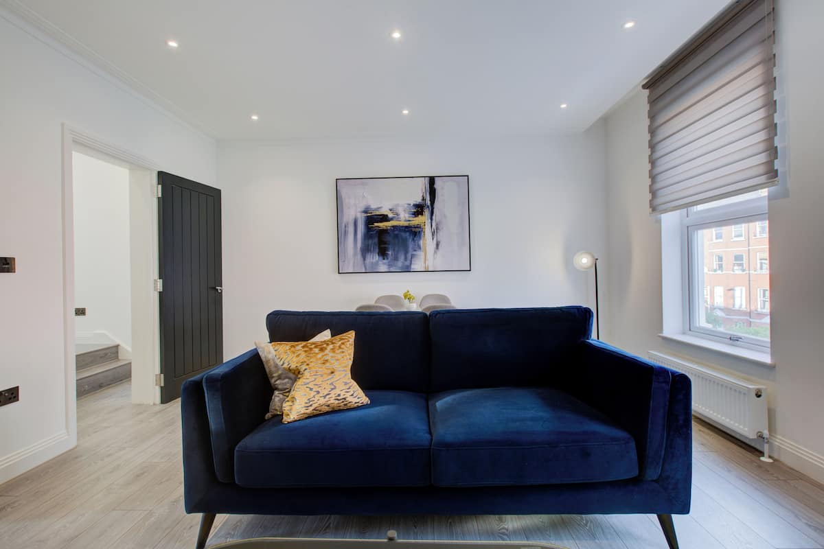 Uma sala de estar moderna com um sofá azul escuro, uma pintura abstrata contemporânea e uma janela com persianas.