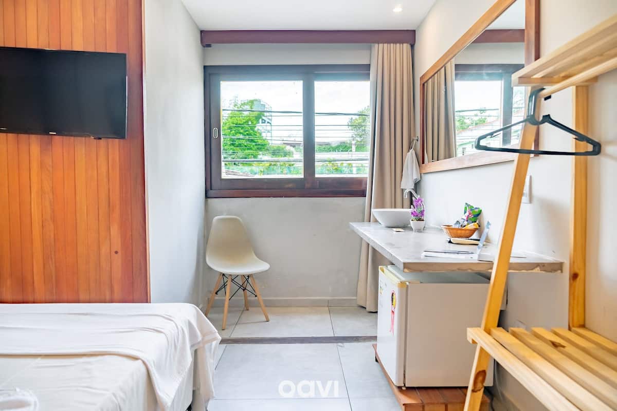 Ett hotellrum med en säng, ett skrivbord, en stol, en TV, ett fönster med utsikt och en spegel.