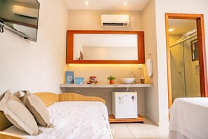 Une chambre d’hôtel de taille réduite, comprenant un lit, un petit réfrigérateur, un lavabo et un miroir au-dessus du comptoir.