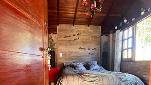 A wooden room with a bed, a wall with a quote, and a window. - Chalé Refúgio 1 (Corumba de Goias)