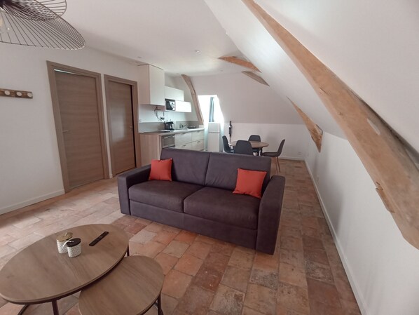 A cozy living area with a sofa, a dining table, and a kitchen in the background.