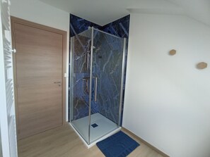 A corner shower with glass doors and a marble wall.