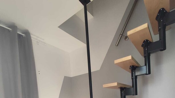 Eine moderne Treppe mit Holzdielen und schwarzen Metallgeländern, die zu einer oberen Etage führt.