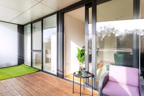 A modern room with large glass doors leading to a balcony, a wooden floor, a green mat, a pink chair, and a small table with a plant and a lantern. - Modern Chiswick Apartment (London)