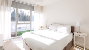 A modern hotel room with a large bed, two bedside tables with lamps, a sliding glass door to a balcony, and a view of the outdoors. - Modern Chiswick Apartment (London)