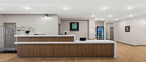 Un comptoir d’accueil moderne, avec un revêtement en bois, un écran numérique et un distributeur automatique en arrière-plan.